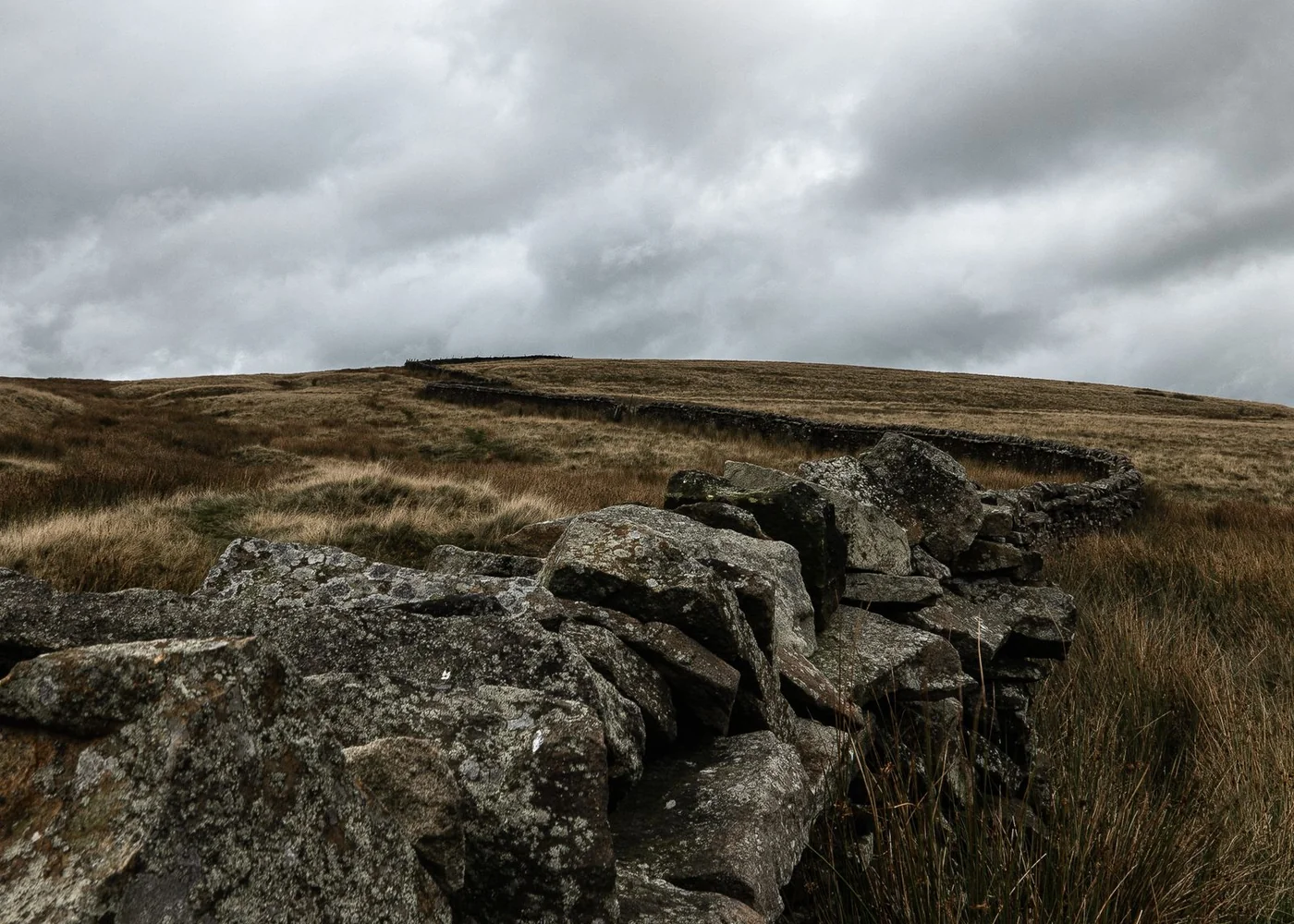 A low stone wall crossing open moorland beneath cloud.