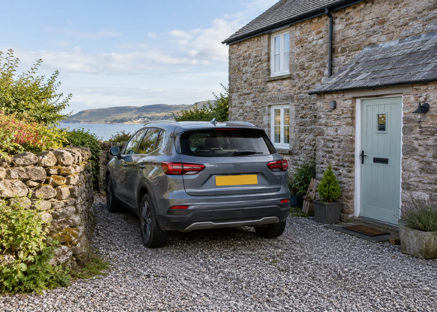 Car parked beside a stone cottage on gravel.