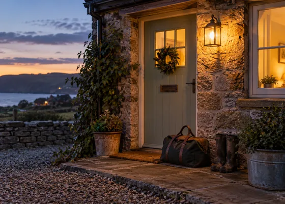 Lit cottage entrance at dusk with a travel bag.